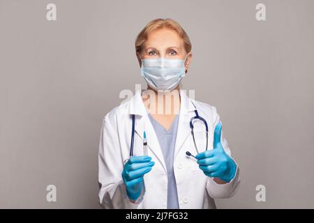 Femme mature infirmière ou médecin tenant la seringue et montrant le pouce vers le haut Banque D'Images