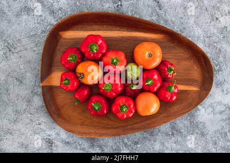 mini-poivrons et tomates fraîchement cueillis dans des tons rouges et orange vifs sur plateau en bois, concept de simples ingrédients naturels sains Banque D'Images