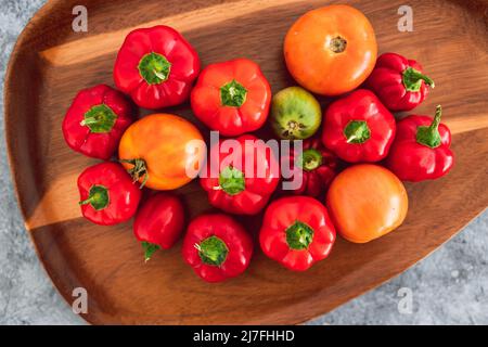 mini-poivrons et tomates fraîchement cueillis dans des tons rouges et orange vifs sur plateau en bois, concept de simples ingrédients naturels sains Banque D'Images