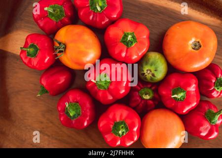 mini-poivrons et tomates fraîchement cueillis dans des tons rouges et orange vifs sur plateau en bois, concept de simples ingrédients naturels sains Banque D'Images