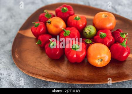 mini-poivrons et tomates fraîchement cueillis dans des tons rouges et orange vifs sur plateau en bois, concept de simples ingrédients naturels sains Banque D'Images