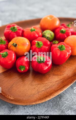 mini-poivrons et tomates fraîchement cueillis dans des tons rouges et orange vifs sur plateau en bois, concept de simples ingrédients naturels sains Banque D'Images