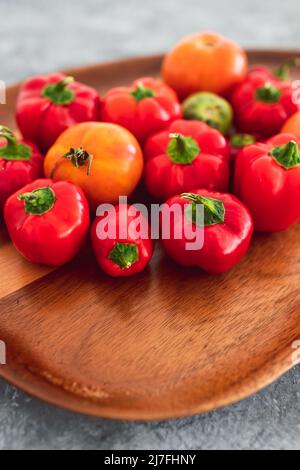 mini-poivrons et tomates fraîchement cueillis dans des tons rouges et orange vifs sur plateau en bois, concept de simples ingrédients naturels sains Banque D'Images