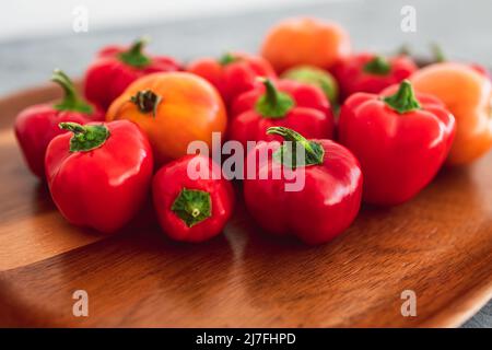 mini-poivrons et tomates fraîchement cueillis dans des tons rouges et orange vifs sur plateau en bois, concept de simples ingrédients naturels sains Banque D'Images