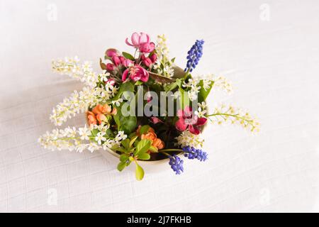 Fleurs printanières délicates dans un vase rond sur une table avec une nappe blanche, un bouquet de pastel et une carte de fleurs délicates Banque D'Images