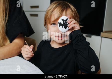 Mignon petit garçon à tête juste tenant une pierre avec une batte peinte sur lui devant son visage. Préparation pour halloween. Banque D'Images