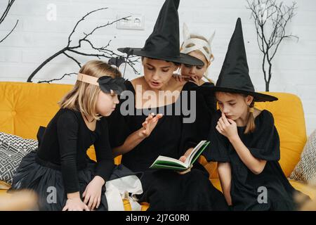 Mère lit l'histoire effrayante aux enfants, ils sont assis sur un canapé. Ils portent tous des costumes pour halloween. Banque D'Images