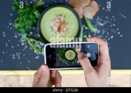 La fille a photographié son déjeuner sur un smartphone. Soupe aux pois verts et aux grains de sarrasin, vue du dessus. Banque D'Images