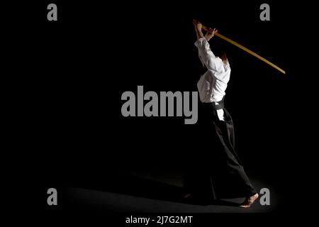 Une fille en hakama noir debout dans la posture de combat avec une épée en bois bokken sur fond noir. Faible profondeur de champ. Banque D'Images