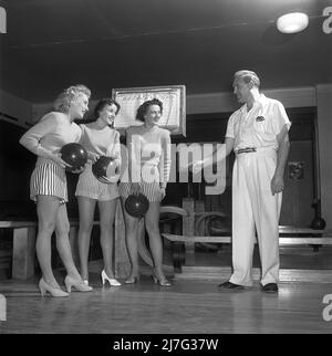 Bowling dans le 1950s. Un homme lance le bowling et trois jeunes femmes se tiennent à côté et regardent. Elles sont vêtues de jupes et de pulls à rayures courtes. Les trois filles sont toutes des actrices de théâtre : Ingrid Björk, UllaCarin Rydén et BRITA Ulfberg. Les spectacles Ewert Ekström les instruit dans le bowling. Il était joueur professionnel de bowling en 1930s et est actuellement instructeur et propriétaire du club de bowling. 1950. Suède Kristoffersson réf. AY36-4 Banque D'Images