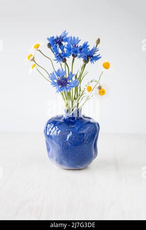 Bouquet de fleurs sauvages dans un vase bleu sur fond blanc en bois Banque D'Images