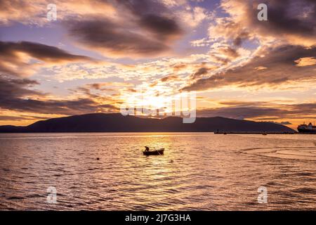 Pêche en mer, pêcheur en bateau, pêche au coucher du soleil, repos actif. Un pêcheur jette une canne à pêche dans l'eau tout en se tenant dans un bateau pendant Banque D'Images
