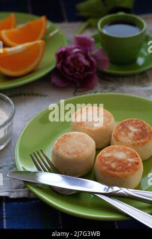 Délicieux cheesecakes diététiques à base de fromage fermier maison pour le petit déjeuner, café noir dans une tasse verte, hachée d'orange et de tulipe pourpre sur un bleu Banque D'Images
