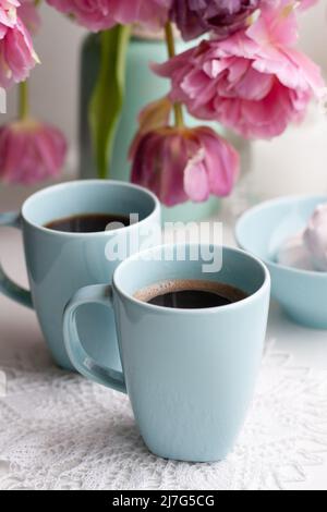 Deux tasses de café noir et un délicat guimauve pour le petit déjeuner sont à côté d'un beau bouquet de tulipes roses dans un vase bleu. Banque D'Images