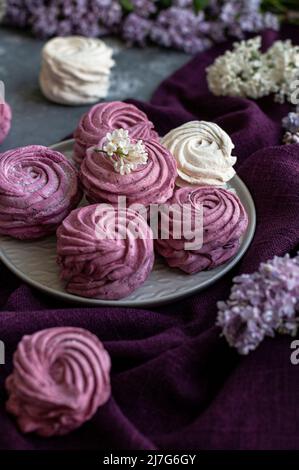 Des guimauves faites maison à base de raisins de Corinthe et de pommes se trouvent sur une assiette entre les inflorescences lilas. Photo dans une touche sombre. Banque D'Images