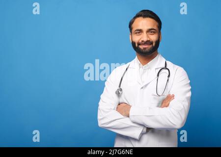 Souriant Indien médecin enfant, physique, thérapeute portant robe médicale blanche avec stéthoscope sur les épaules, les bras croisés isolés sur bleu, espace de copie. Santé et médecine Banque D'Images