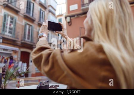 Vue arrière de la femme blonde tenant son smartphone à l'extérieur Banque D'Images