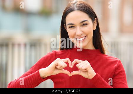 Vue de face portrait d'une femme heureuse en forme de coeur avec les mains dans la rue Banque D'Images