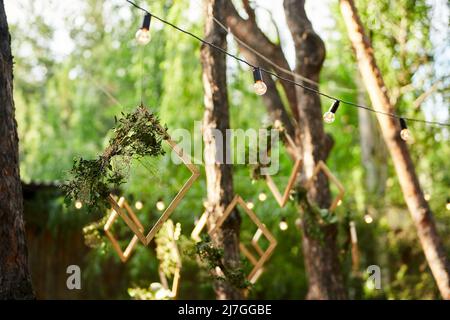 Réception de mariage à l'extérieur dans la forêt de pins. Tables à manger, bancs décorés dans le style boho avec bougies, fleurs, lumières de fée printanière, assiettes Banque D'Images