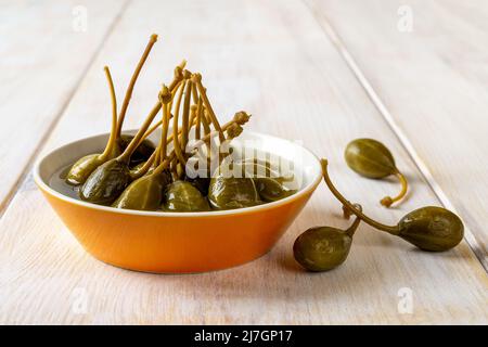 De savoureuses baies de câpres marinées dans un bol d'orange sur une table en bois blanc. Les fruits à câpres marinés sont l'ingrédient commun de la cuisine méditerranéenne. Caperberry. Banque D'Images