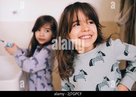 Bonne fille debout avec une sœur tenant une brosse à dents dans la salle de bains Banque D'Images