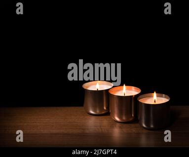 Trois pots en métal cuivrés avec bougies allumées, disposés sur une surface en bois avec un espace pour les copies noires Banque D'Images