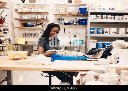 Portrait complet d'une femme souriante assise à table en classe artistique Banque D'Images