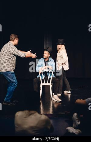 Longueur complète de l'homme guidant l'artiste assis sur une chaise tout en répétant avec une femme sur scène Banque D'Images