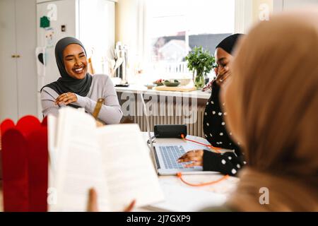 Jeune femme gaie portant le hijab assis avec des amis à la table Banque D'Images