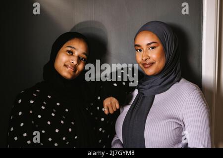 Jeunes femmes souriantes portant des hijabs debout devant le mur à la maison Banque D'Images