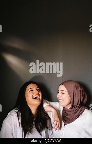 Bonne jeune femme portant le hijab regardant l'ami rire sur fond gris Banque D'Images