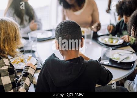 Vue arrière d'un garçon assis avec des amis à la table de la cafétéria Banque D'Images