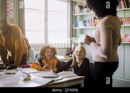 Des élèves souriants qui interagissent avec un enseignant en classe à l'école Banque D'Images