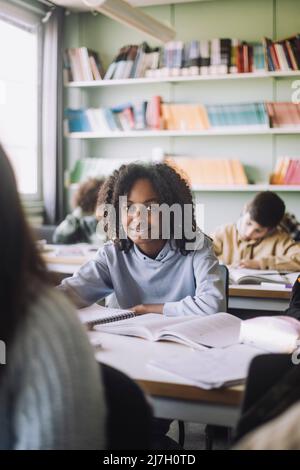 Fille avec des livres assis au bureau dans la salle de classe Banque D'Images
