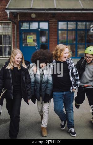 Des amis multiraciaux joueurs qui marchent en quittant l'école Banque D'Images