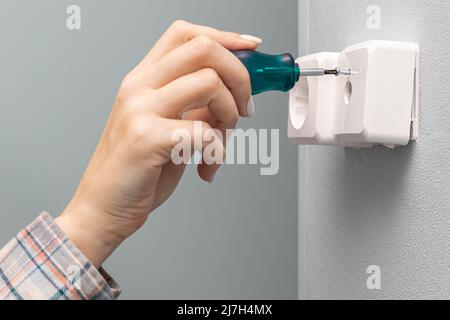 une femme se dévisse avec un tournevis pour réparer une prise murale de télévision. Photo de haute qualité Banque D'Images