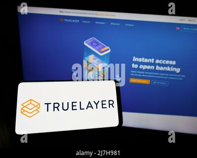 Personne tenant un smartphone avec le logo de la société britannique TrueLayer Limited à l'écran devant le site Web. Mise au point sur l'affichage du téléphone. Banque D'Images