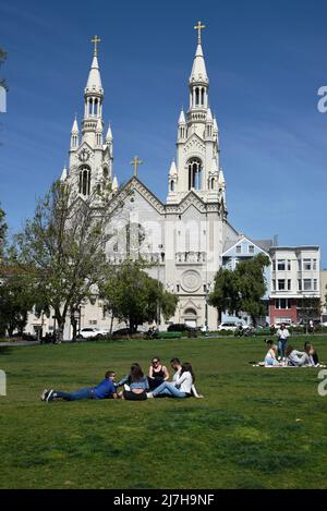 Un homme portant une veste de moto Hell's Angels marche son chien devant l'église catholique Saints Pierre et Paul à San Francisco, en Californie. Banque D'Images