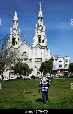 Un homme portant une veste de moto Hell's Angels marche son chien devant l'église catholique Saints Pierre et Paul à San Francisco, en Californie. Banque D'Images