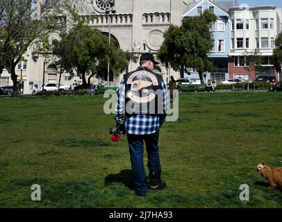 Un homme portant une veste de moto Hell's Angels marche son chien devant l'église catholique Saints Pierre et Paul à San Francisco, en Californie. Banque D'Images