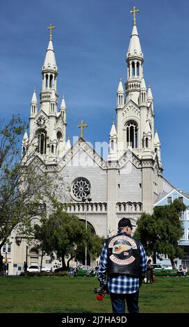 Un homme portant une veste de moto Hell's Angels marche son chien devant l'église catholique Saints Pierre et Paul à San Francisco, en Californie. Banque D'Images