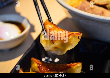 Les baguettes ramassent des gyoza frits (boulettes) de style japonais d'une assiette noire. Banque D'Images