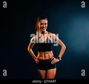 Portrait d'une jeune femme musclée gaie dans des vêtements de sport posant sur fond noir Banque D'Images