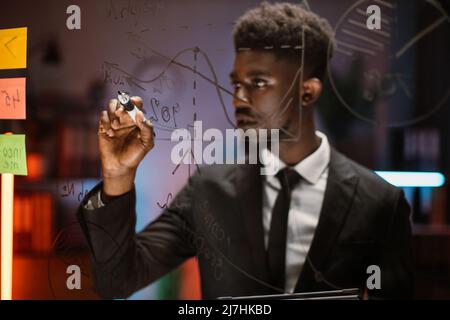 Gros plan portrait flou d'un jeune homme afro-américain beau, écrivant sur une planche de verre et faisant l'analyse du plan de projet. Économie, commerce, finance et concept d'entreprise Banque D'Images