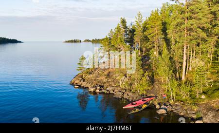 Des kayaks touristiques se tiennent au bord de la côte rocheuse pittoresque avec une forêt de pins. Une île magnifique dans un grand lac lors d'une chaude soirée d'été. Vue aérienne. Banque D'Images