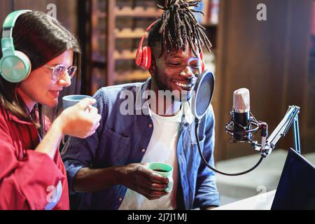 Couple multiethnique de jeunes qui parlent en utilisant des microphones avec antipop pour enregistrer une session de podcast vidéo en direct en streaming en ligne - 20s contenu creat Banque D'Images