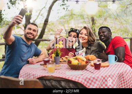 Amis multiraciaux se détendant en prenant le selfie à la table de pique-nique - les jeunes s'amusent ensemble en célébrant un brunch à l'extérieur à la campagne t Banque D'Images