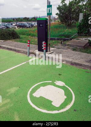 Station électrique pour voiture électrique EV avec logo clignotant. Point de charge utilisé pour fournir de l'énergie renouvelable à bas prix aux véhicules, contre le terrain de coquelicots sur le parking ouvert à Thessalonique, Grèce. Banque D'Images