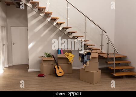 Pile de boîtes en carton avec guitare, livres et vêtements par escalier dans la nouvelle maison vide, espace de copie Banque D'Images