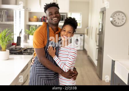Portrait d'un jeune homme afro-américain joyeux portant un tablier embrassant une jeune amie dans la cuisine Banque D'Images